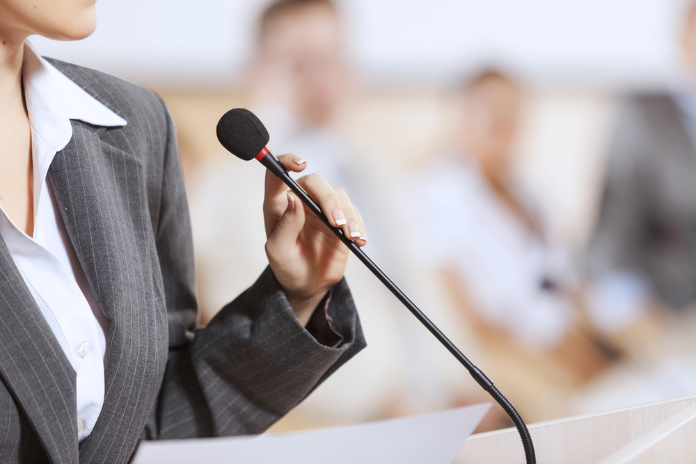 Businesswoman standing on stage and reporting for audience Businesswoman standing on stage and reporting for audience